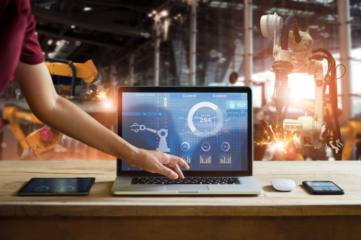 Someone controlling machinery in the background with a laptop in the foreground showing data and controls. The influx of business intelligence from IoT is another reason why cyber security must support business intelligence.
