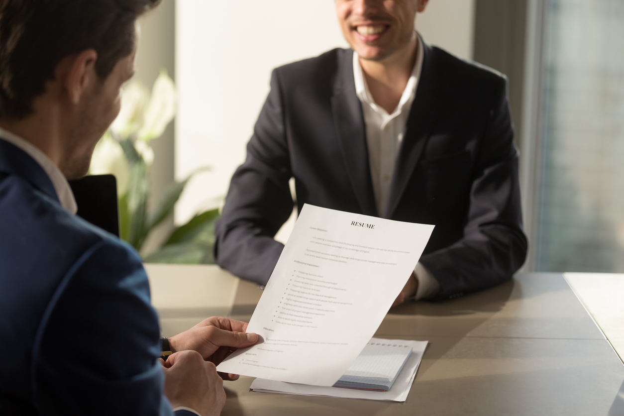 An interviewer and interviewee smiling at one another across a desk. Access to exclusive hiring opportunities is one of the benefits of having a security clearance.
