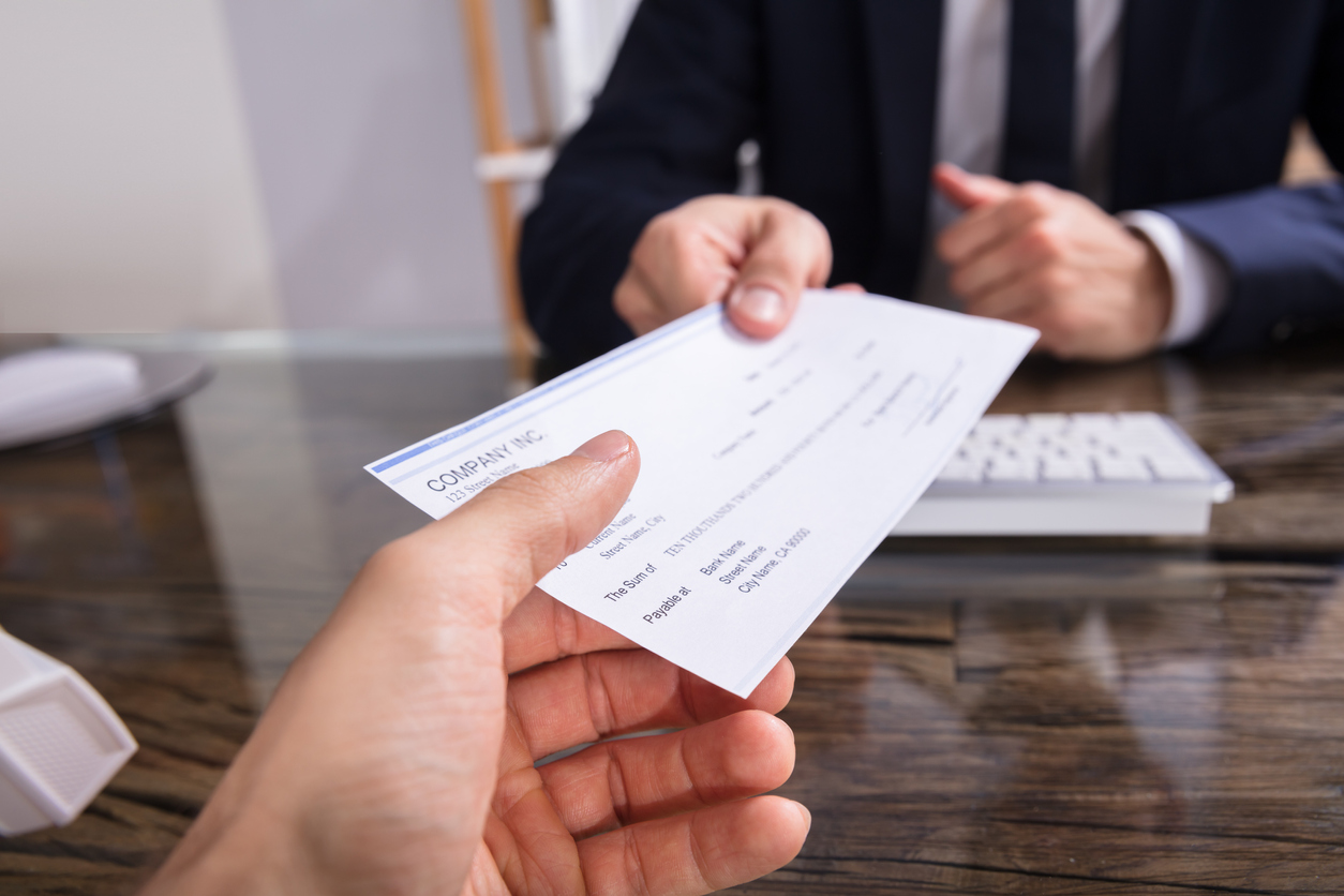 An employer handing a pay check to an employee. Increased earning potential is one of the benefits of having a security clearance.