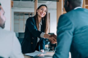 An employee referral case study symbolized by a recruiter shaking hands with a candidate while an employee sits beside the candidate.